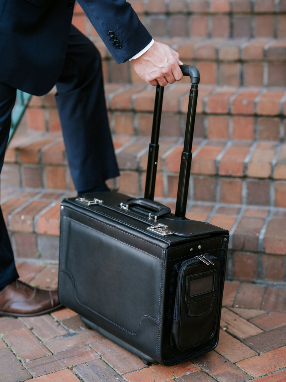 Black Person in a suit holding a black suitcase catalog case lawyer case on a brick pavement